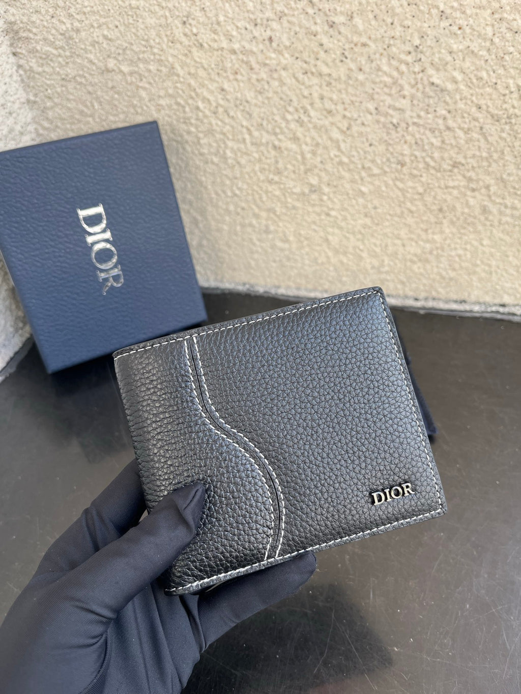 Dior small leather wallet, textured dark exterior with curved stitched panel and logo.