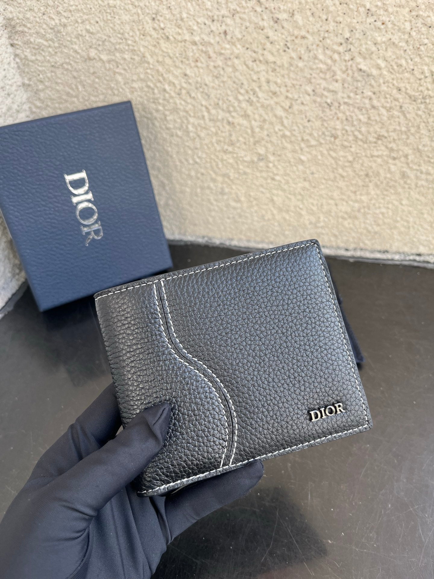 Dior small leather wallet, textured dark exterior with curved stitched panel and logo.