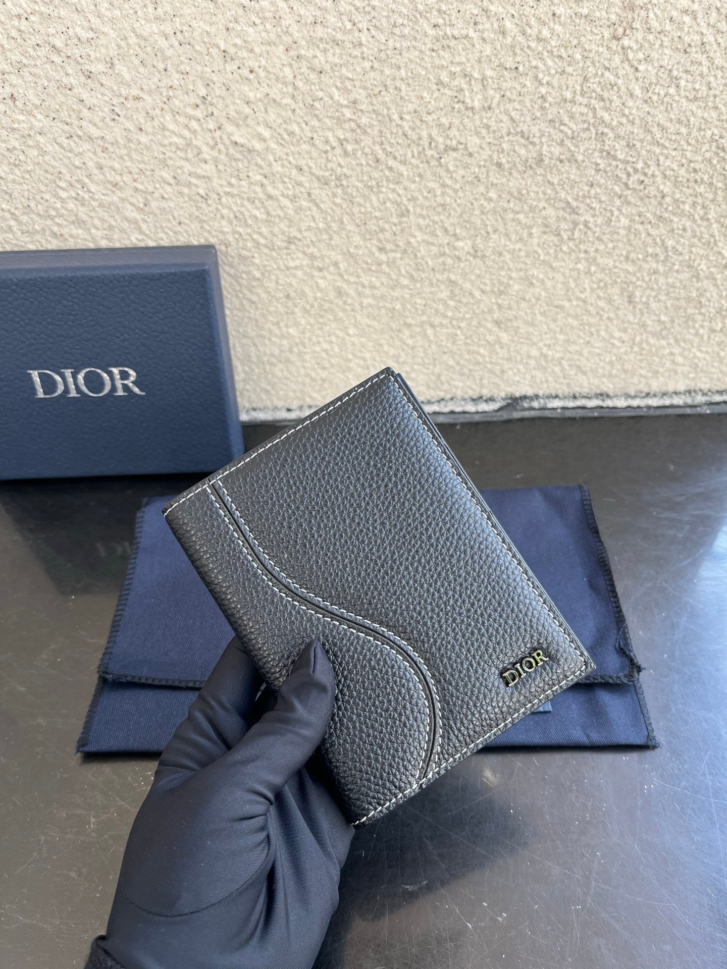 Dior card holder in dark textured leather, side view with stitched curved flap and logo.