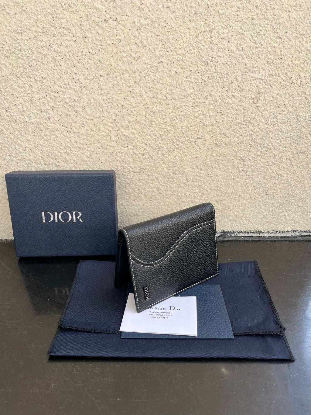 Dior card holder in dark textured leather with curved flap and small Dior logo.