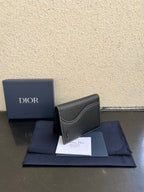 Dior card holder in dark textured leather with curved flap and small Dior logo.