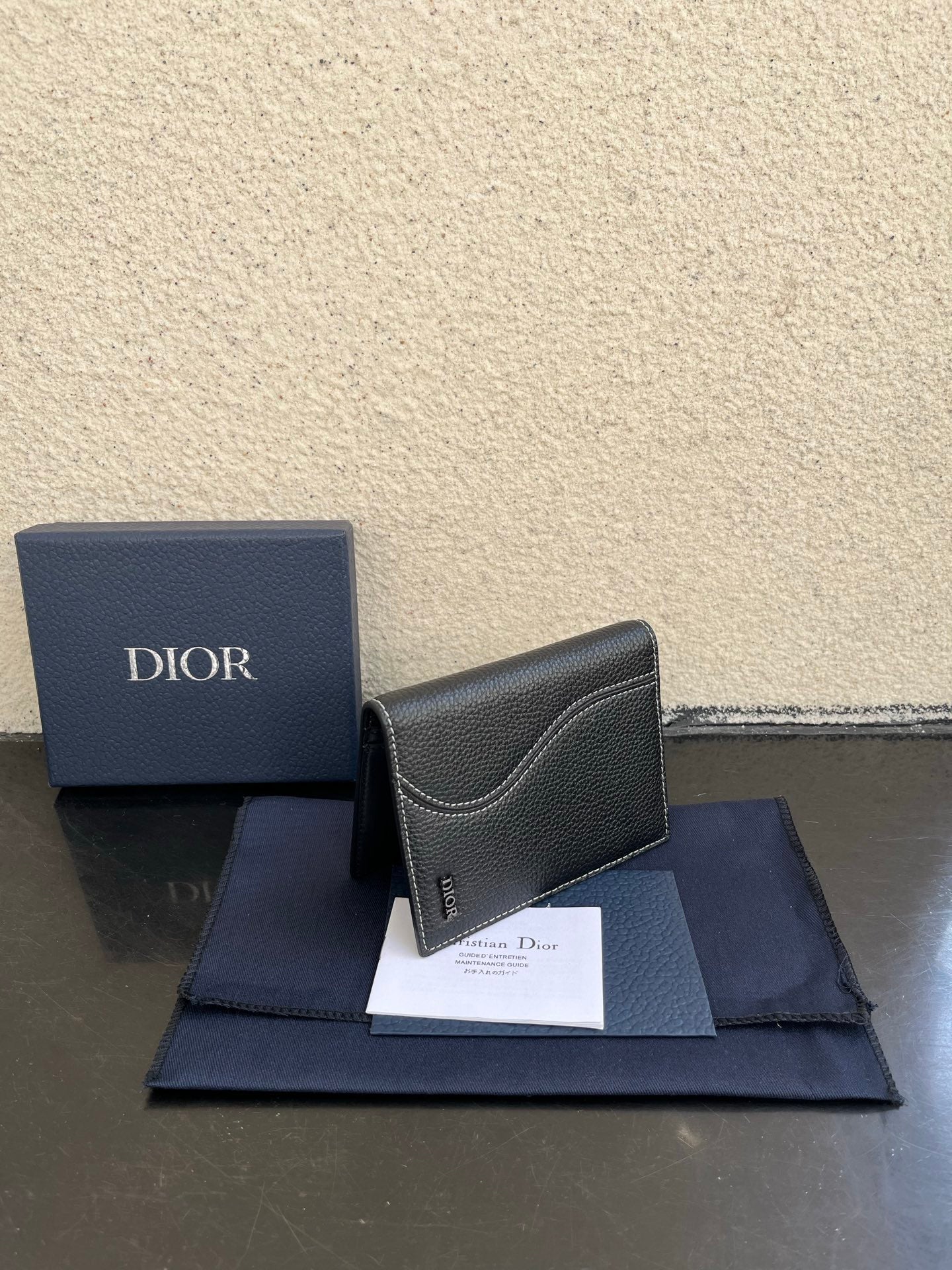 Dior card holder in dark textured leather with curved flap and small Dior logo.