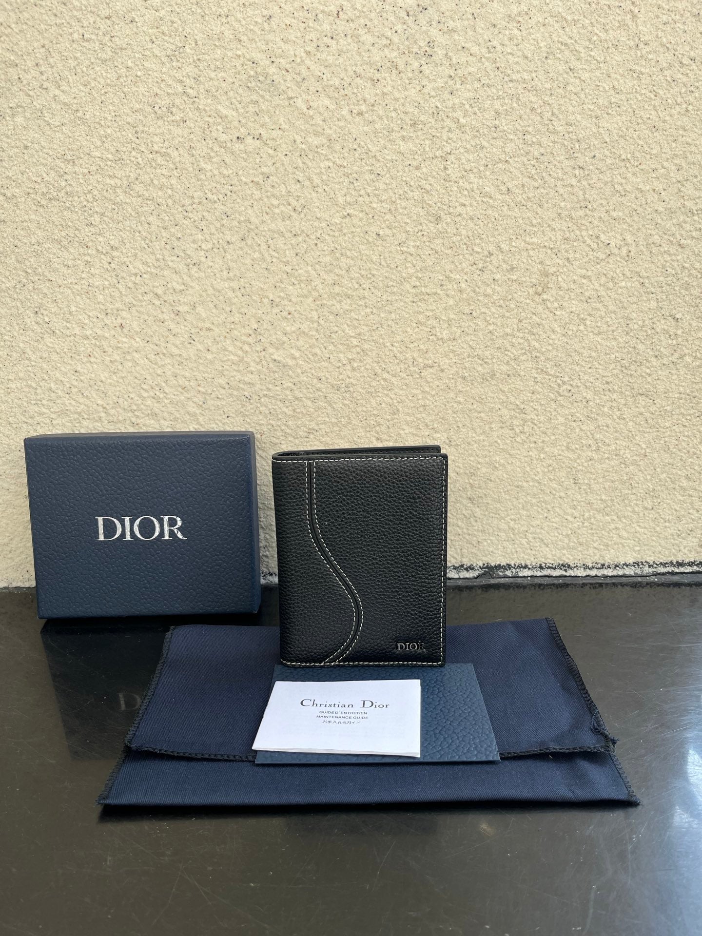 Dior card holder in dark textured leather with curved flap detail and Dior logo.