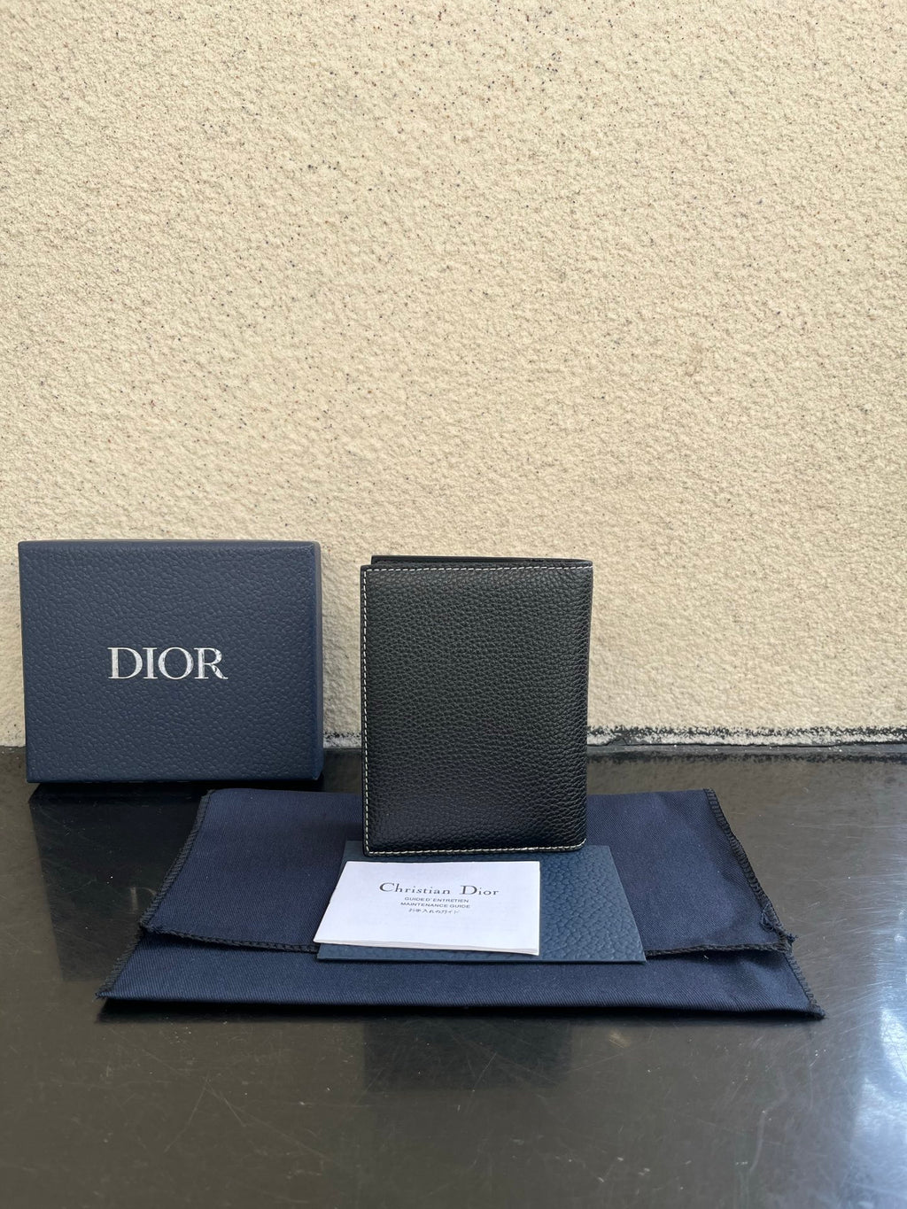 Dior card holder in dark textured leather, upright view with flap and Dior branding.