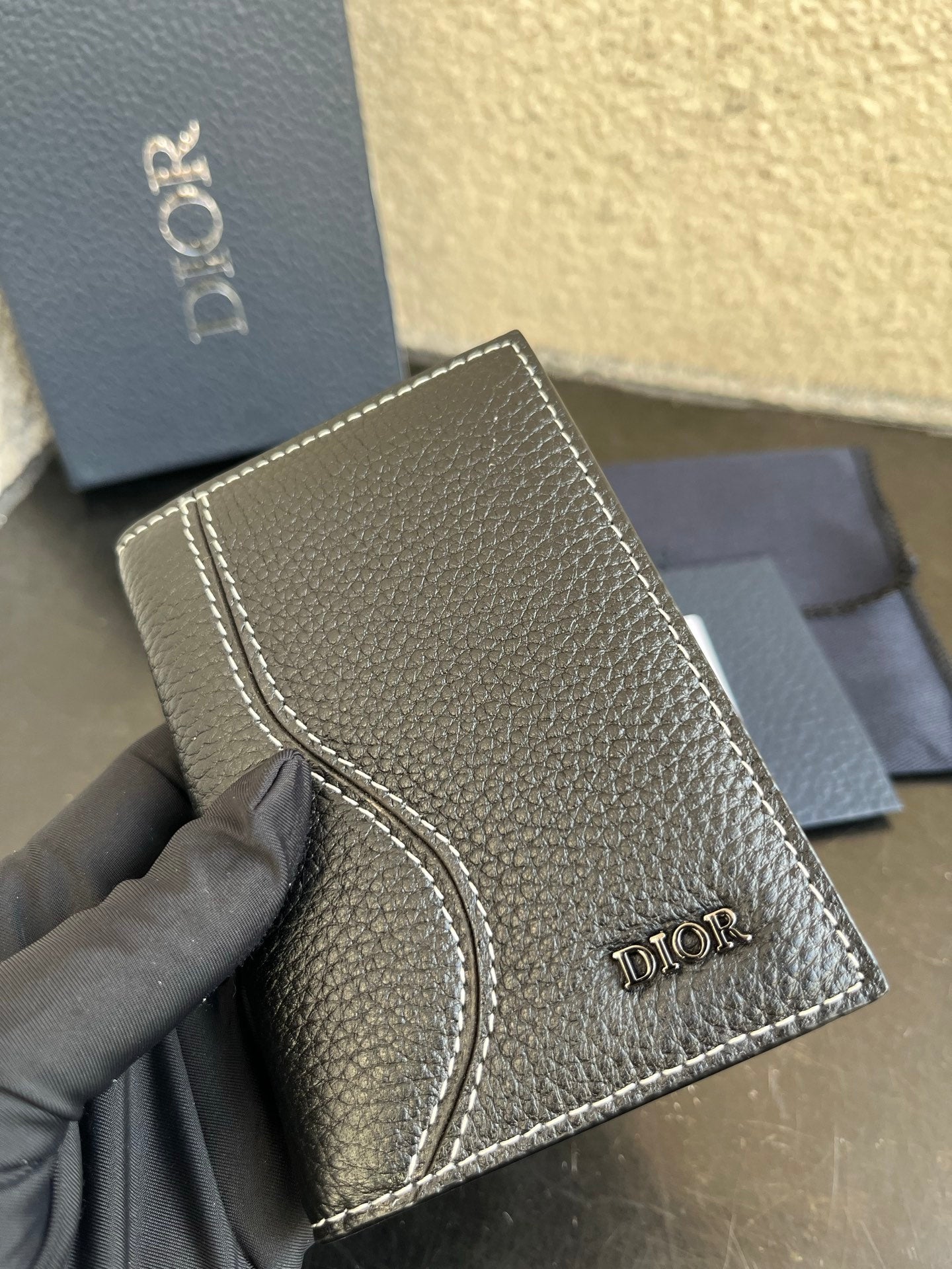Small bag closeup: textured dark leather wallet with stitched edge and Dior logo