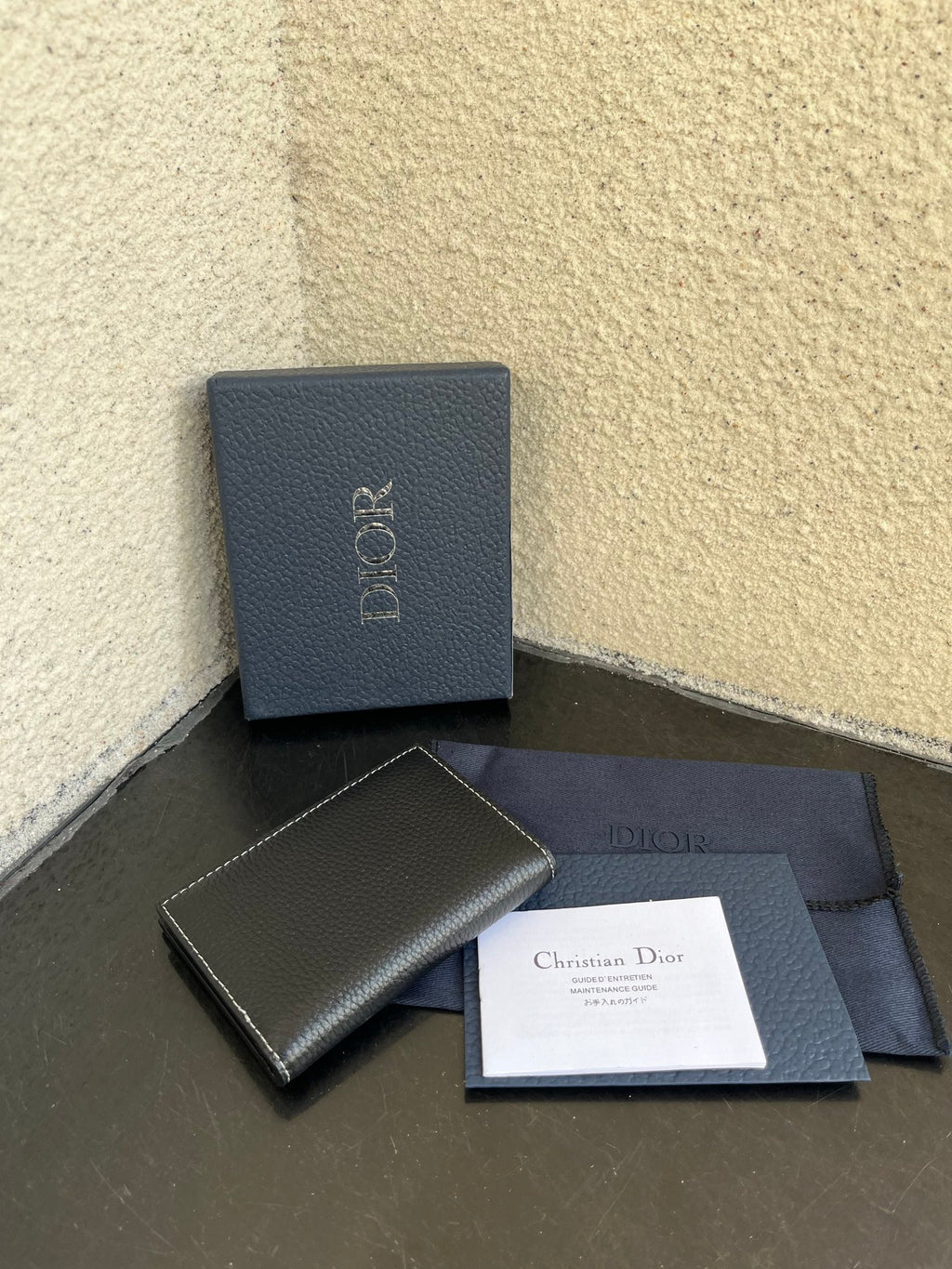 Small bag with dark leather compact wallet, Dior box, and papers on cloth