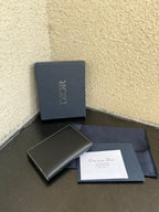 Small bag with dark leather compact wallet, Dior box, and papers on cloth