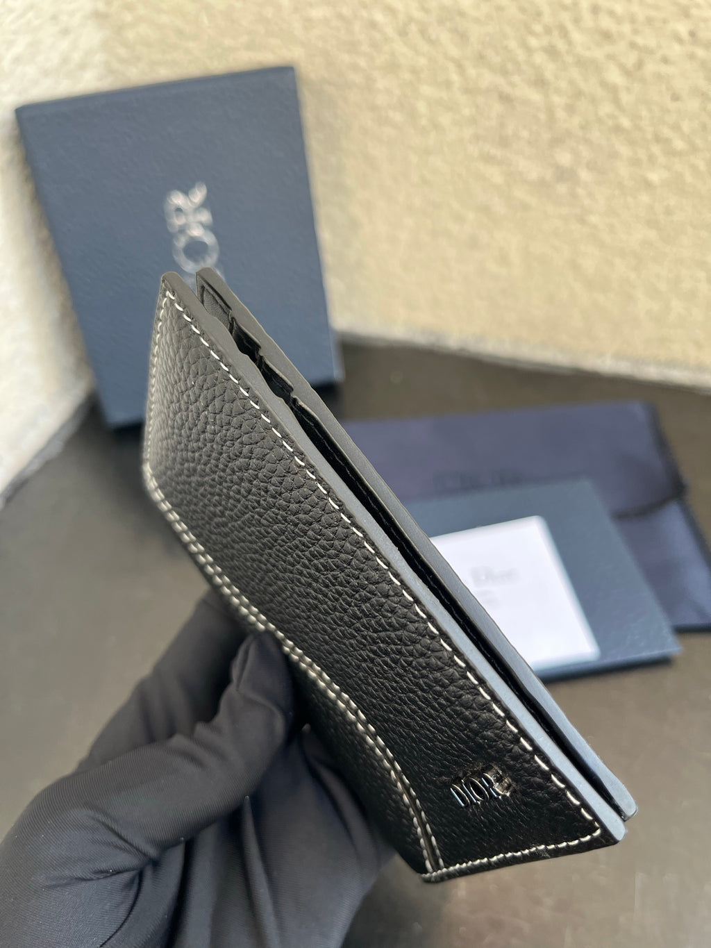 Small bag side view: dark leather wallet with contrast stitching and Dior branding