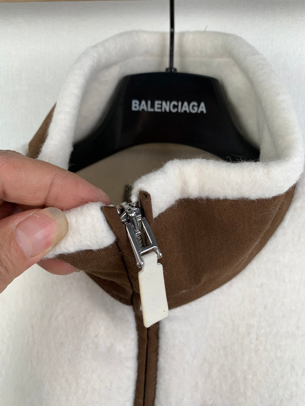 Hand adjusting zipper pull on cream fleece quarter-zip jacket with brown placket