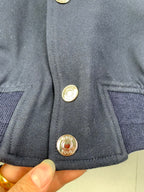 Close-up of navy jacket front with gold snap buttons and logo medallions
