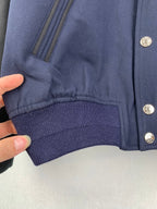 Lower front of navy jacket with welt pocket opening and ribbed knit hem trim
