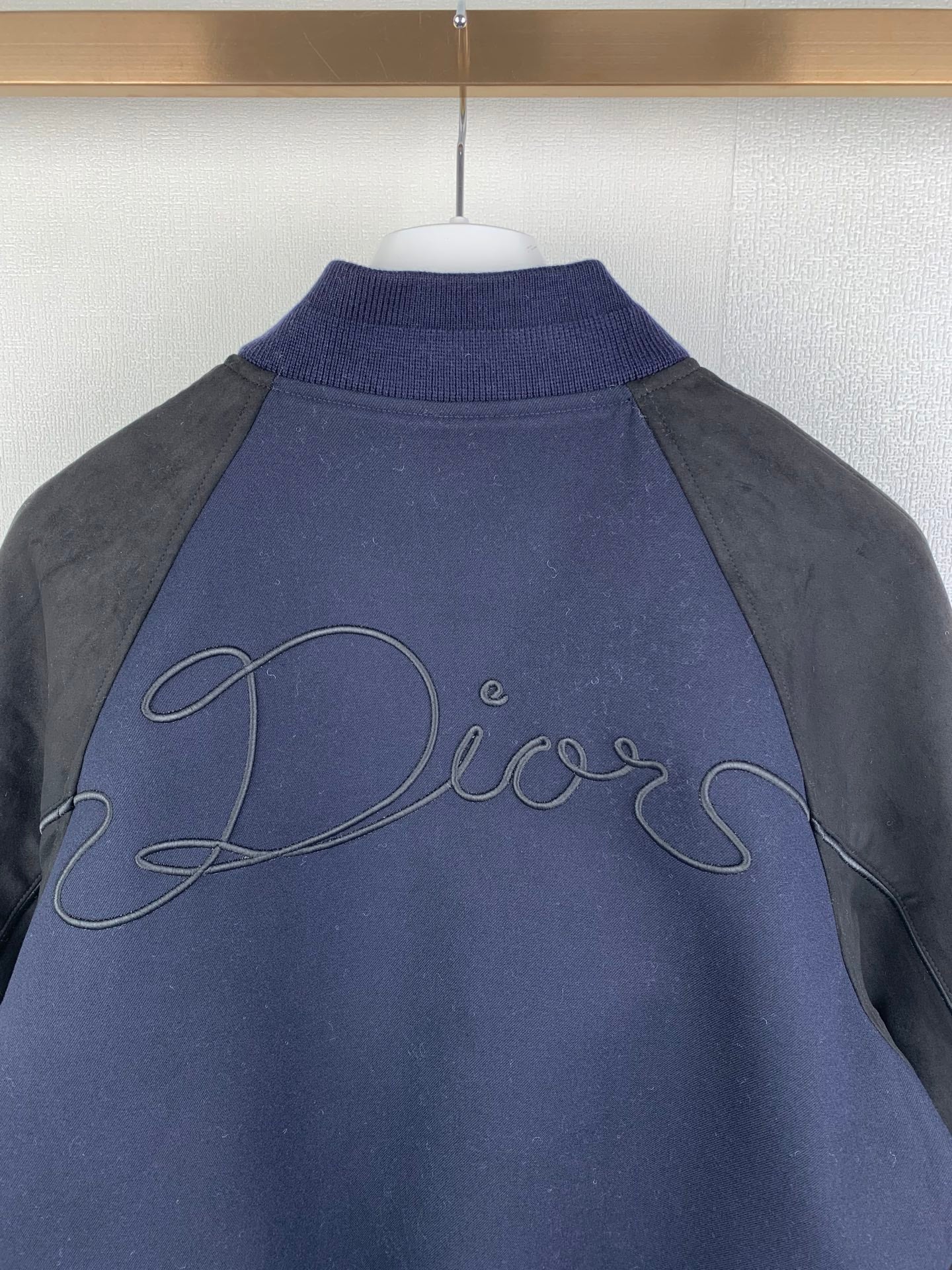 Back collar area of dark navy jacket with gray sleeves, Dior script embroidery on yoke