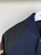 Shoulder and side panel of navy jacket with gray sleeve overlay, ribbed stand collar