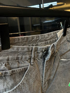 Close-up of light gray denim pants waist with logo patch and green cross
