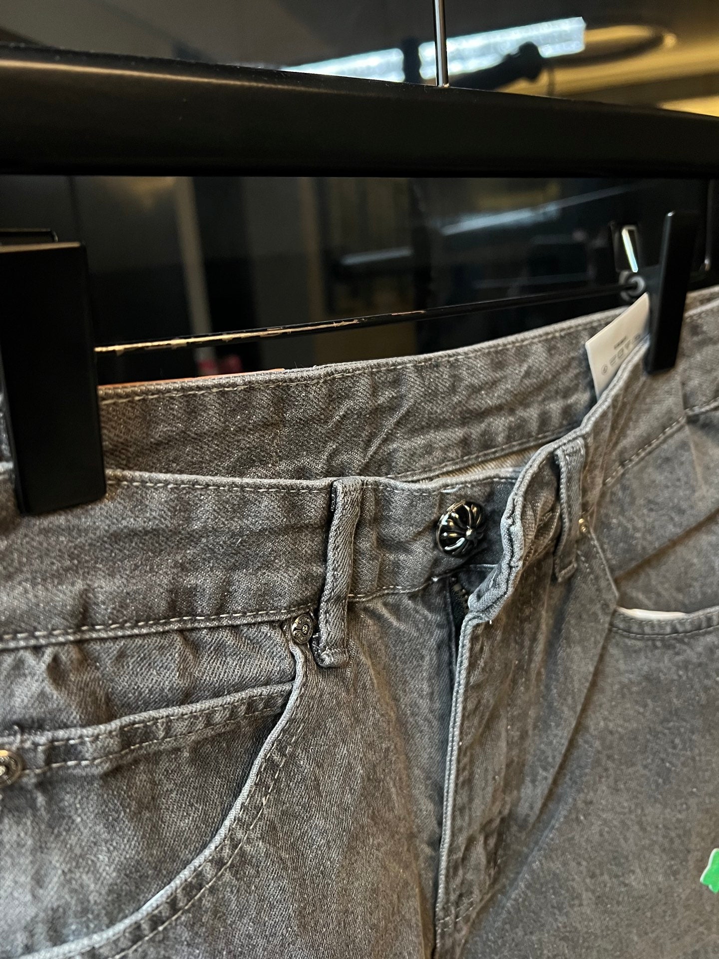 Close-up of light gray denim pants waist with logo patch and green cross