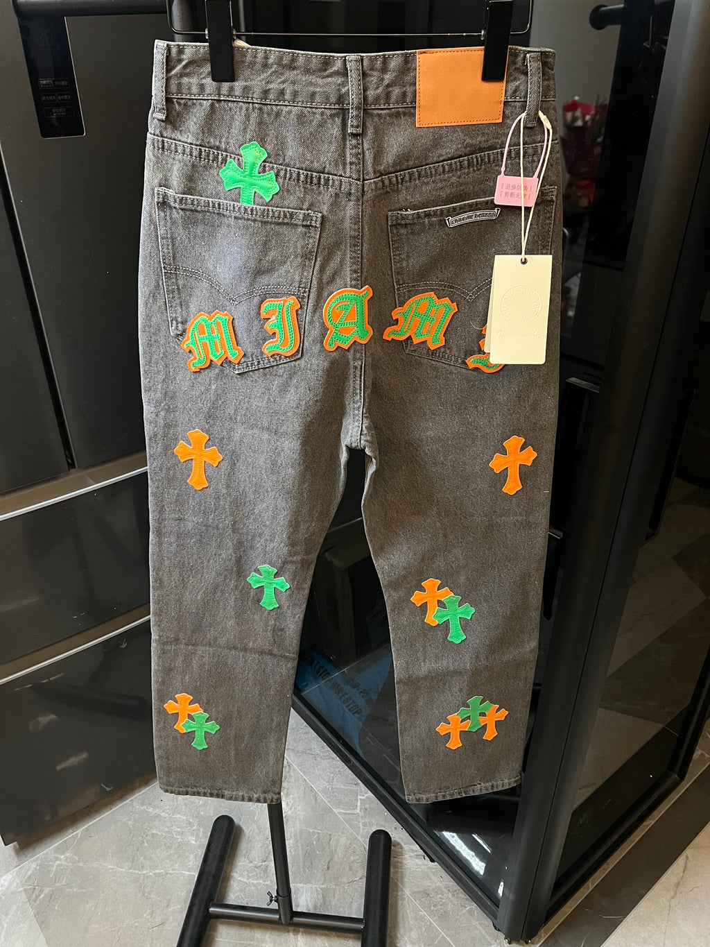 Light gray denim pants with colorful cross and letter-style patches on the back