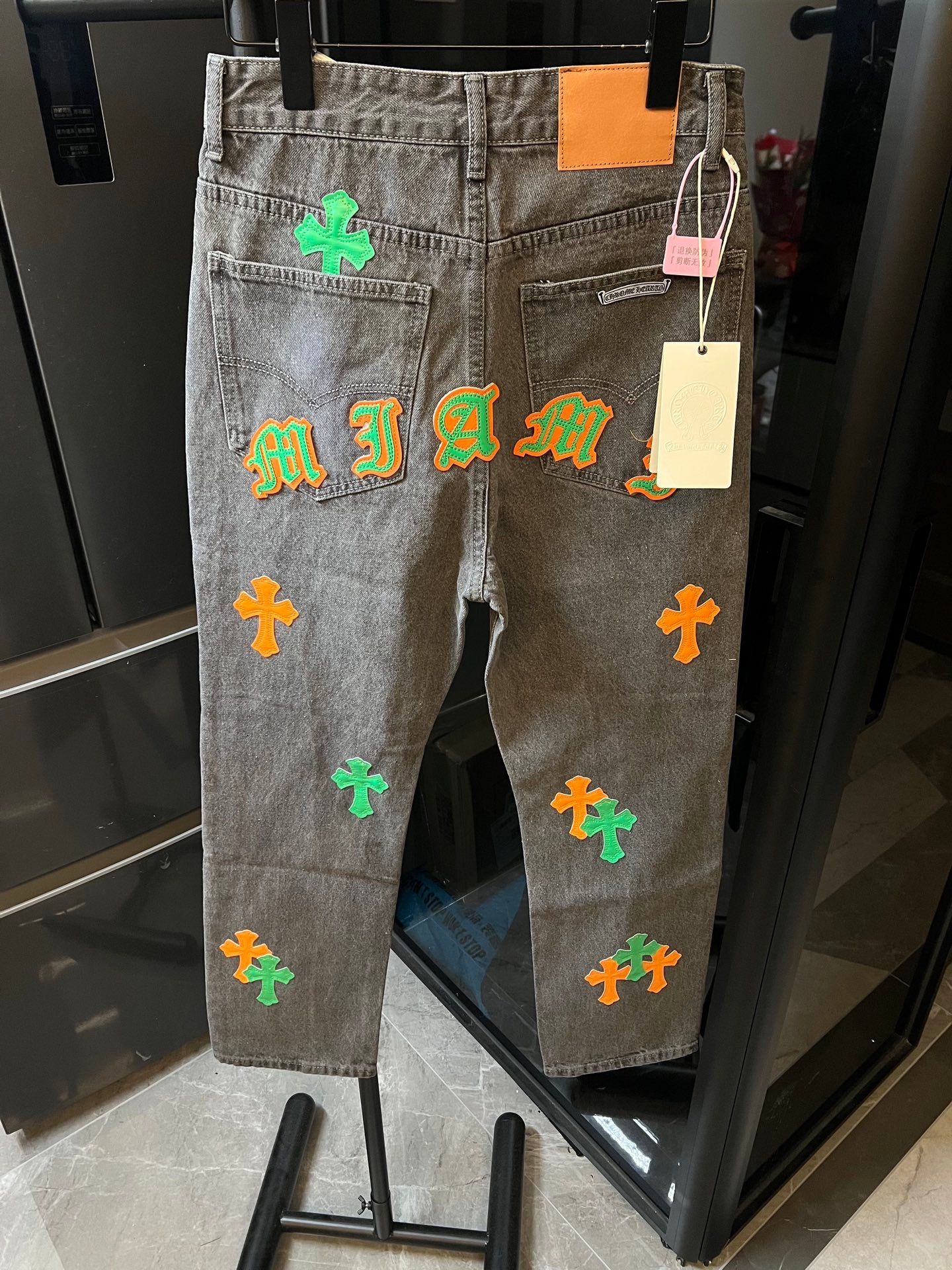 Light gray denim pants with colorful cross and letter-style patches on the back