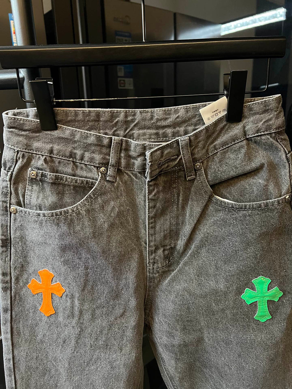 Front view of light gray denim pants with colorful cross patch on the thigh