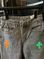 Front view of light gray denim pants with colorful cross patch on the thigh