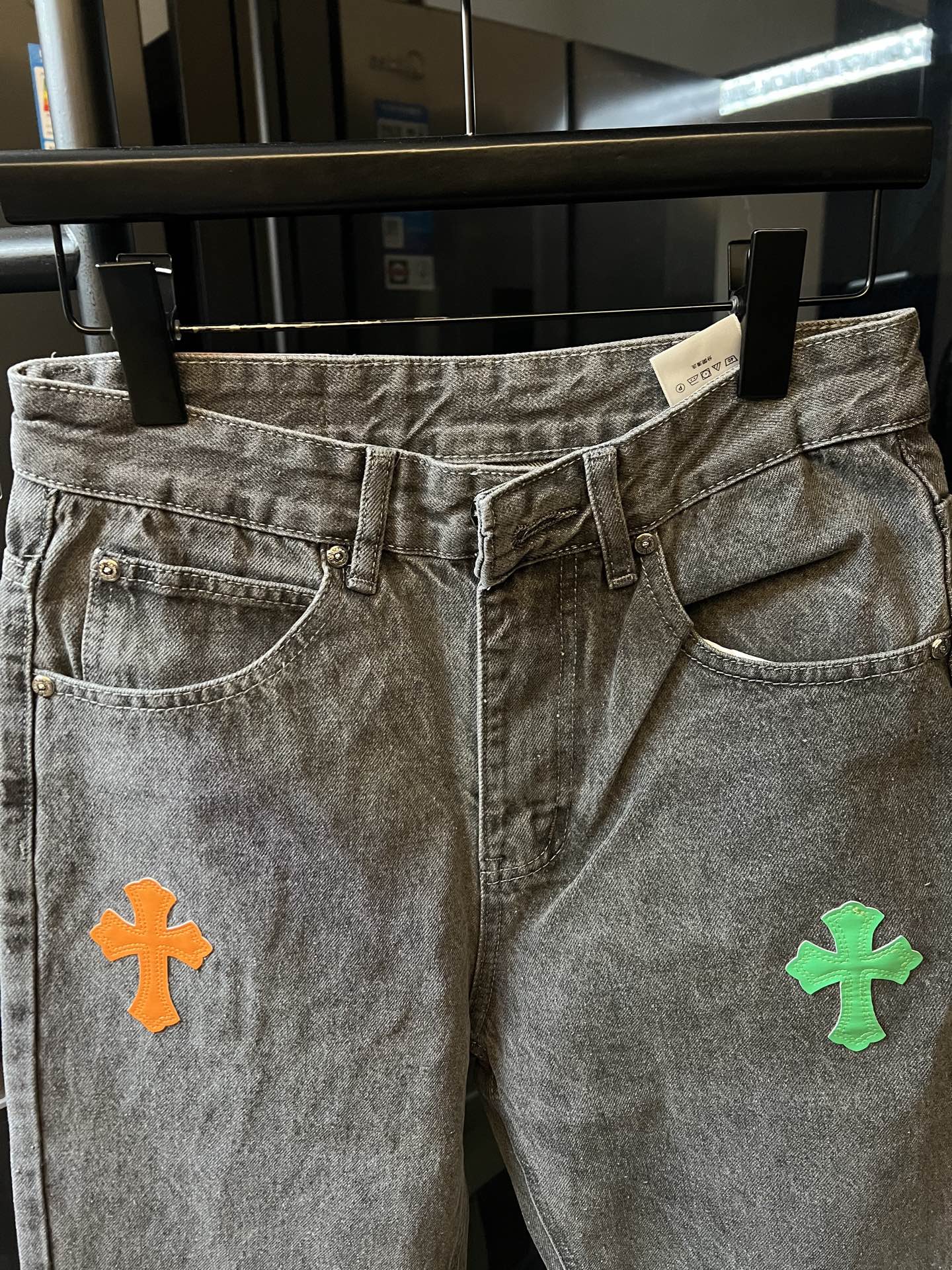 Front view of light gray denim pants with colorful cross patch on the thigh