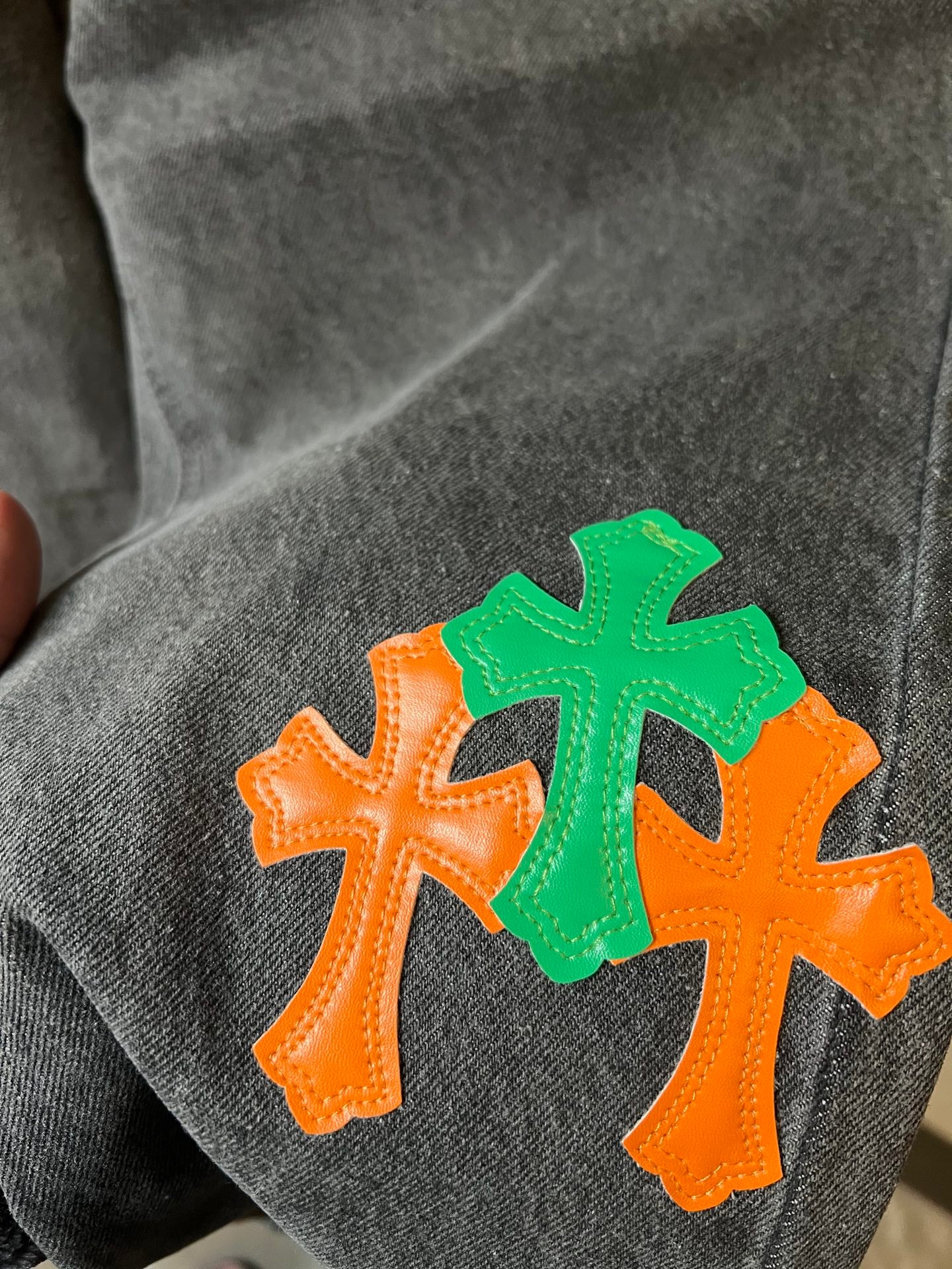 Light gray denim pants fabric detail with orange and green cross appliques
