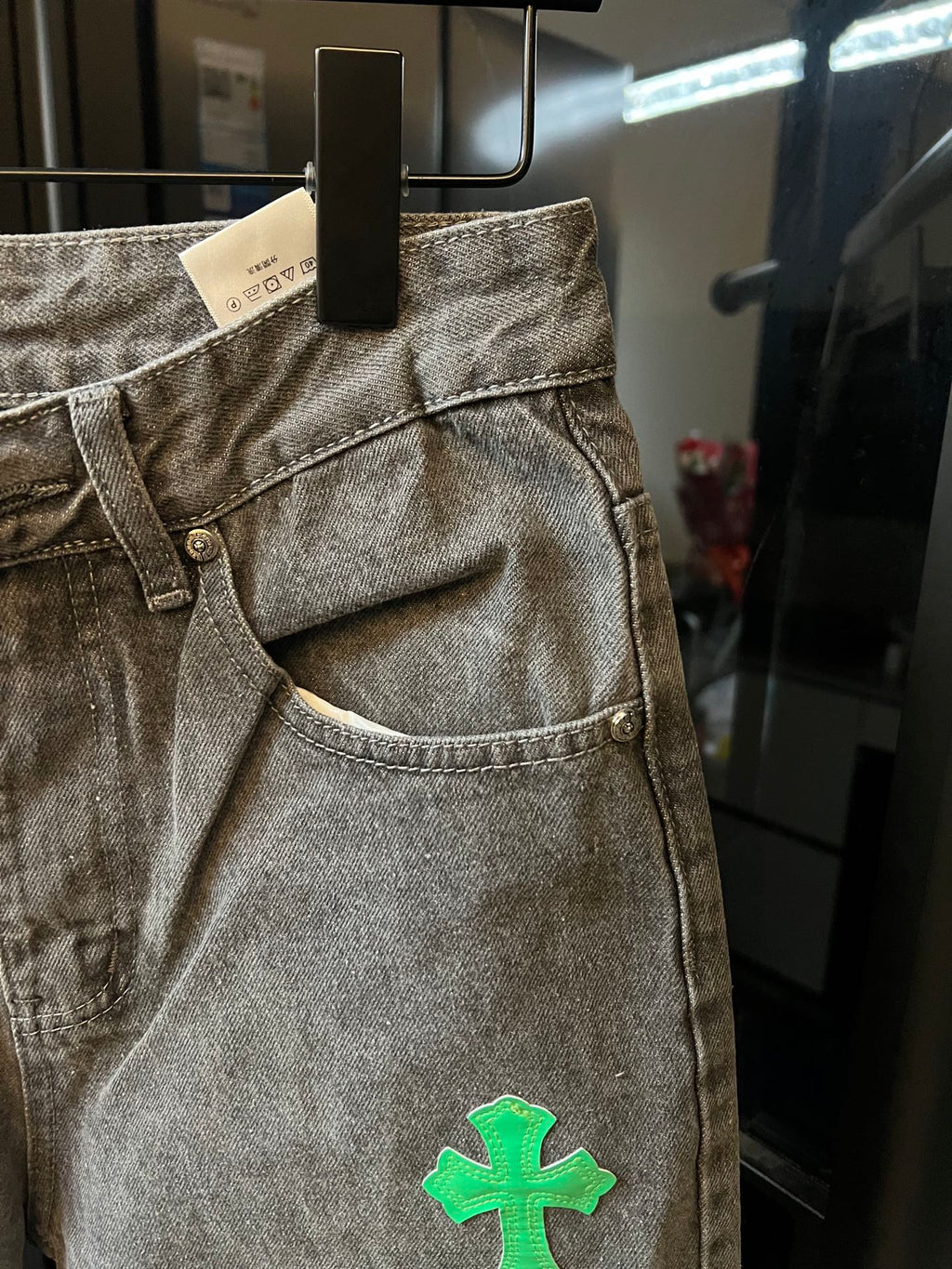 Light gray denim pants with front fly and green cross patch on the leg