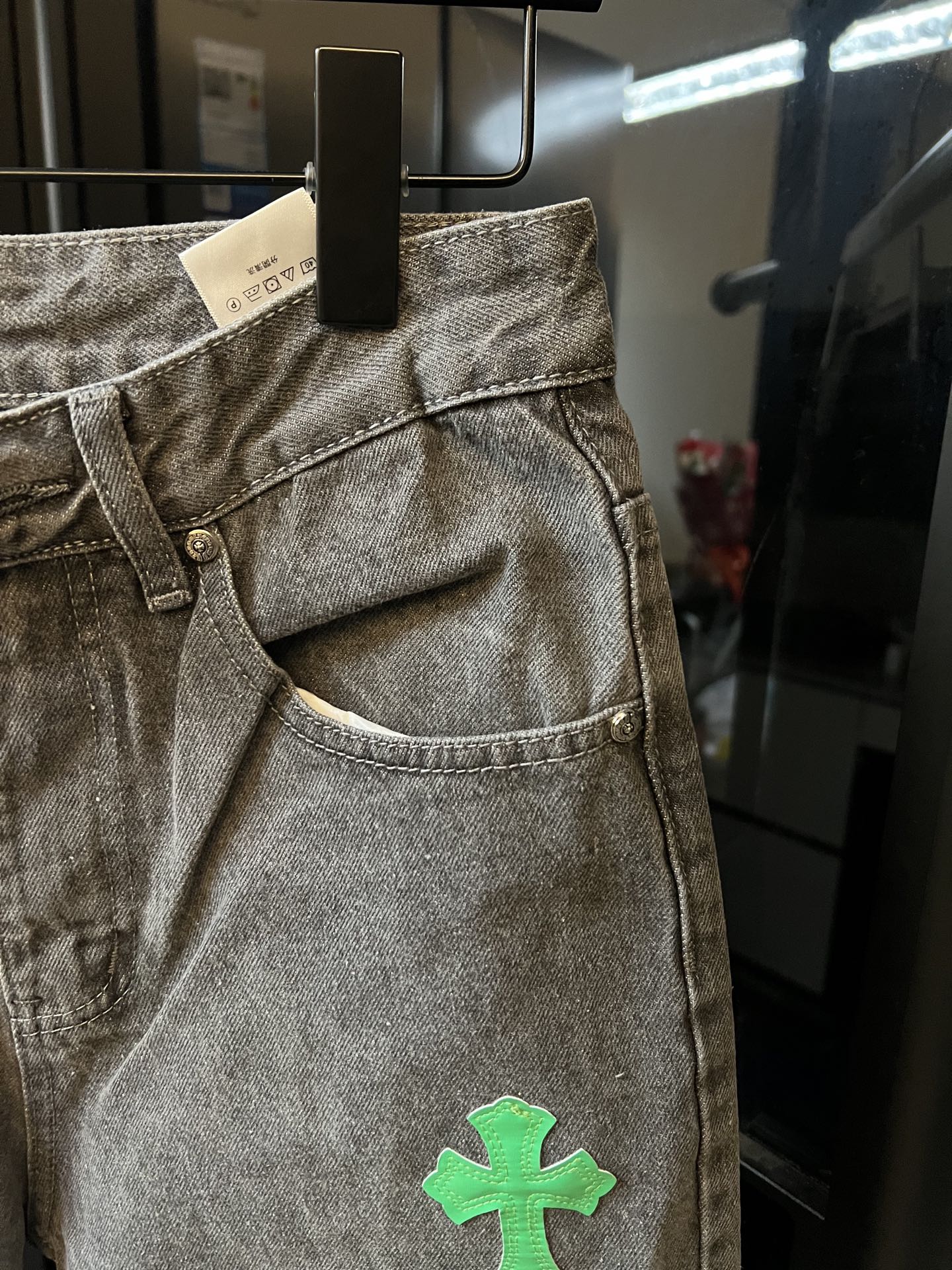 Light gray denim pants with front fly and green cross patch on the leg
