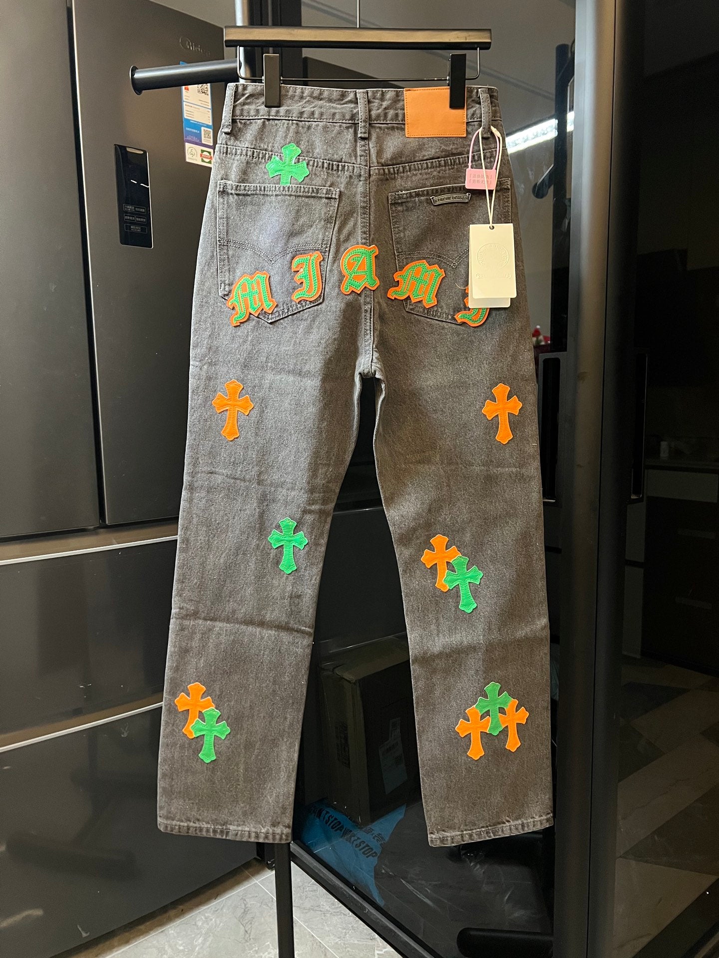 Light gray denim pants with neon cross and letter-style patches on the front
