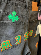 Light gray denim pants close-up with green cross and multi-color letter-style patches