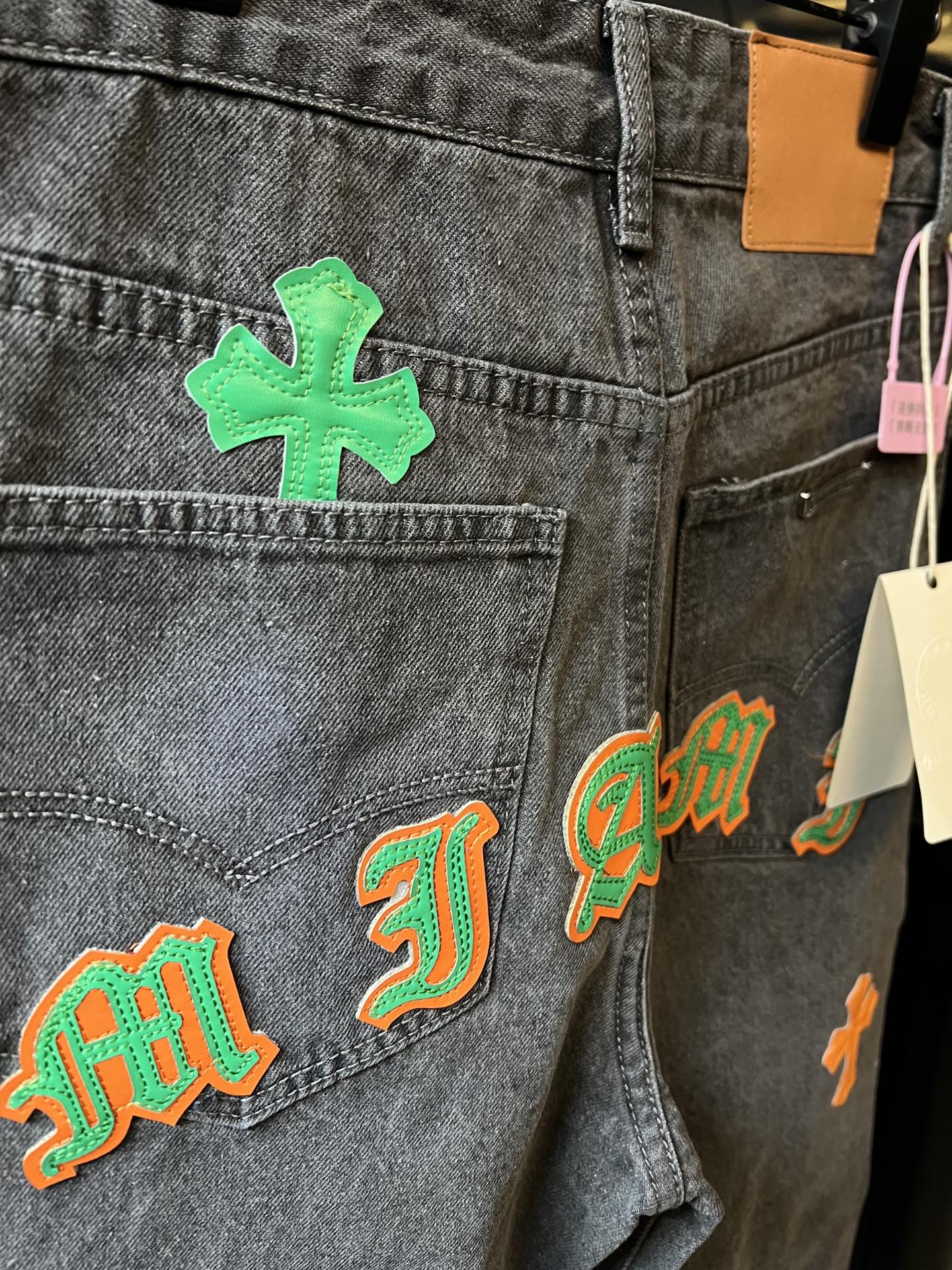 Light gray denim pants close-up with green cross and multi-color letter-style patches