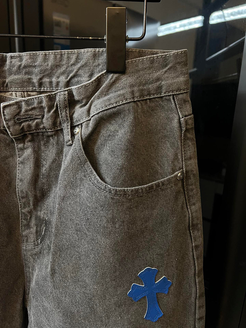 Light gray denim pants with blue cross patch near pocket, zip-fly front