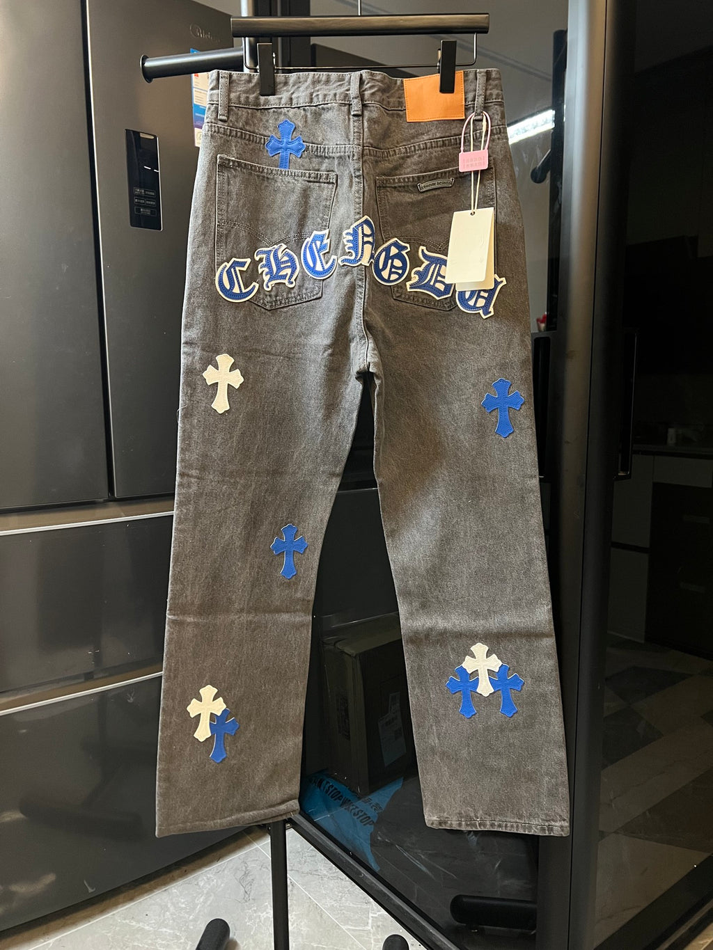 Light gray denim pants with blue cross patches and printed lettering across front