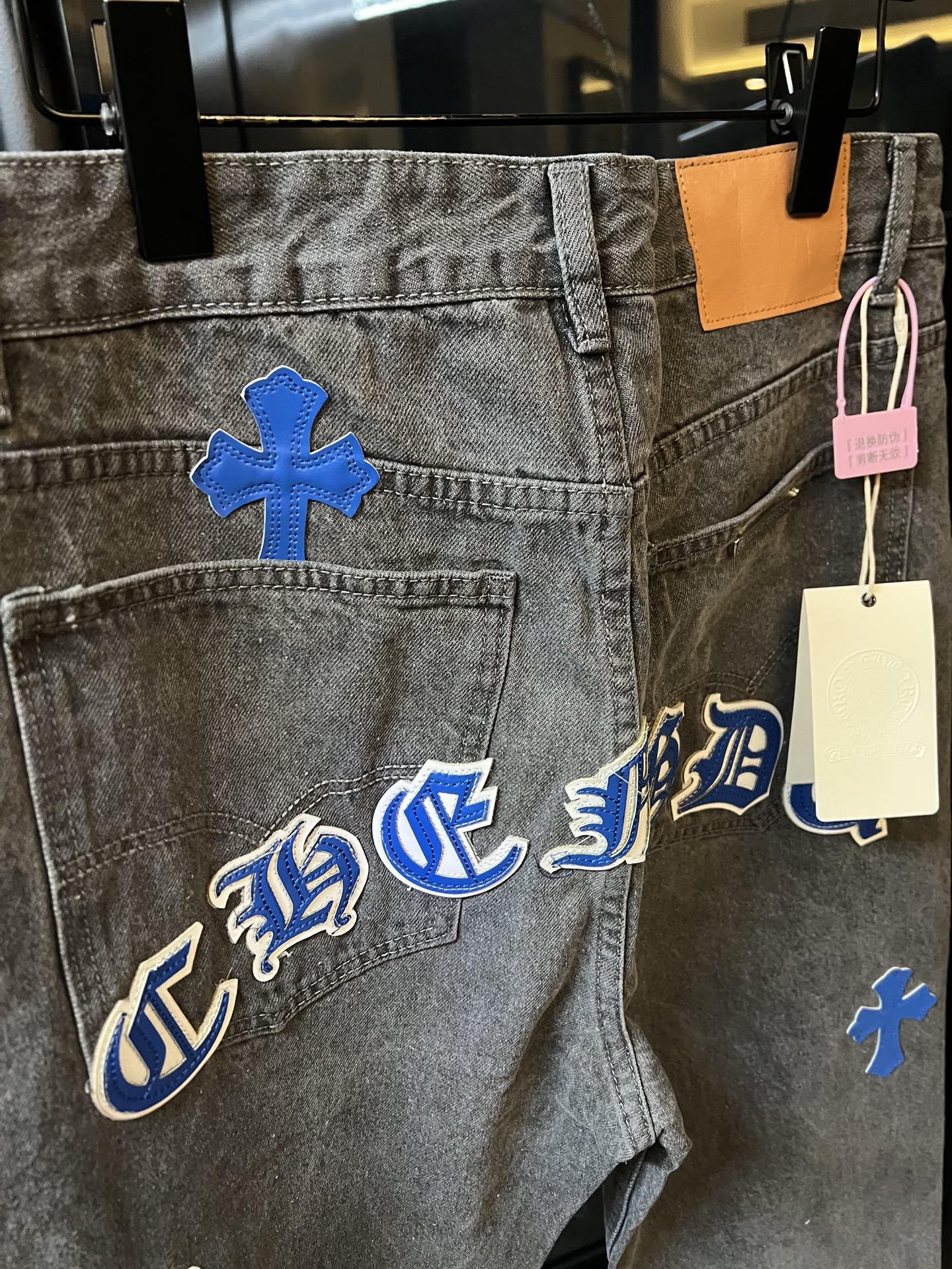 Light gray denim pants with blue gothic-style lettering and cross patches