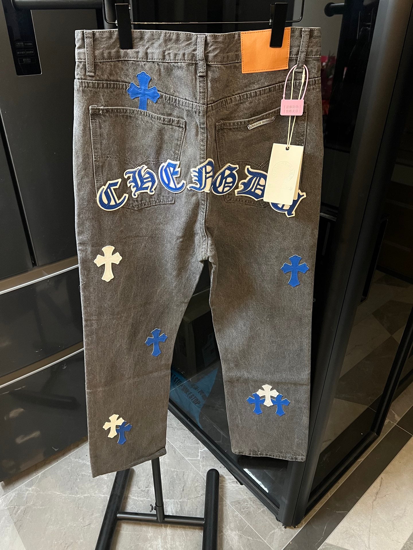 Light gray denim pants with blue cross patches and gothic-style lettering on back