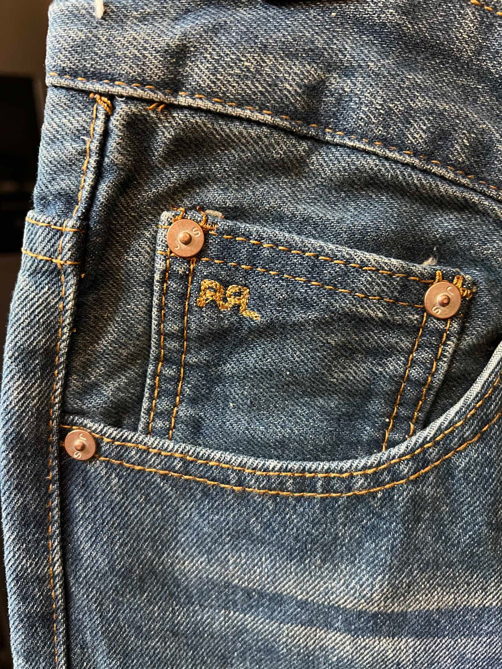 Light blue denim jeans with stitched coin pocket and copper-tone buttons