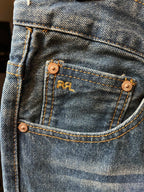 Light-wash denim jeans close-up of coin pocket with brass buttons and stitching