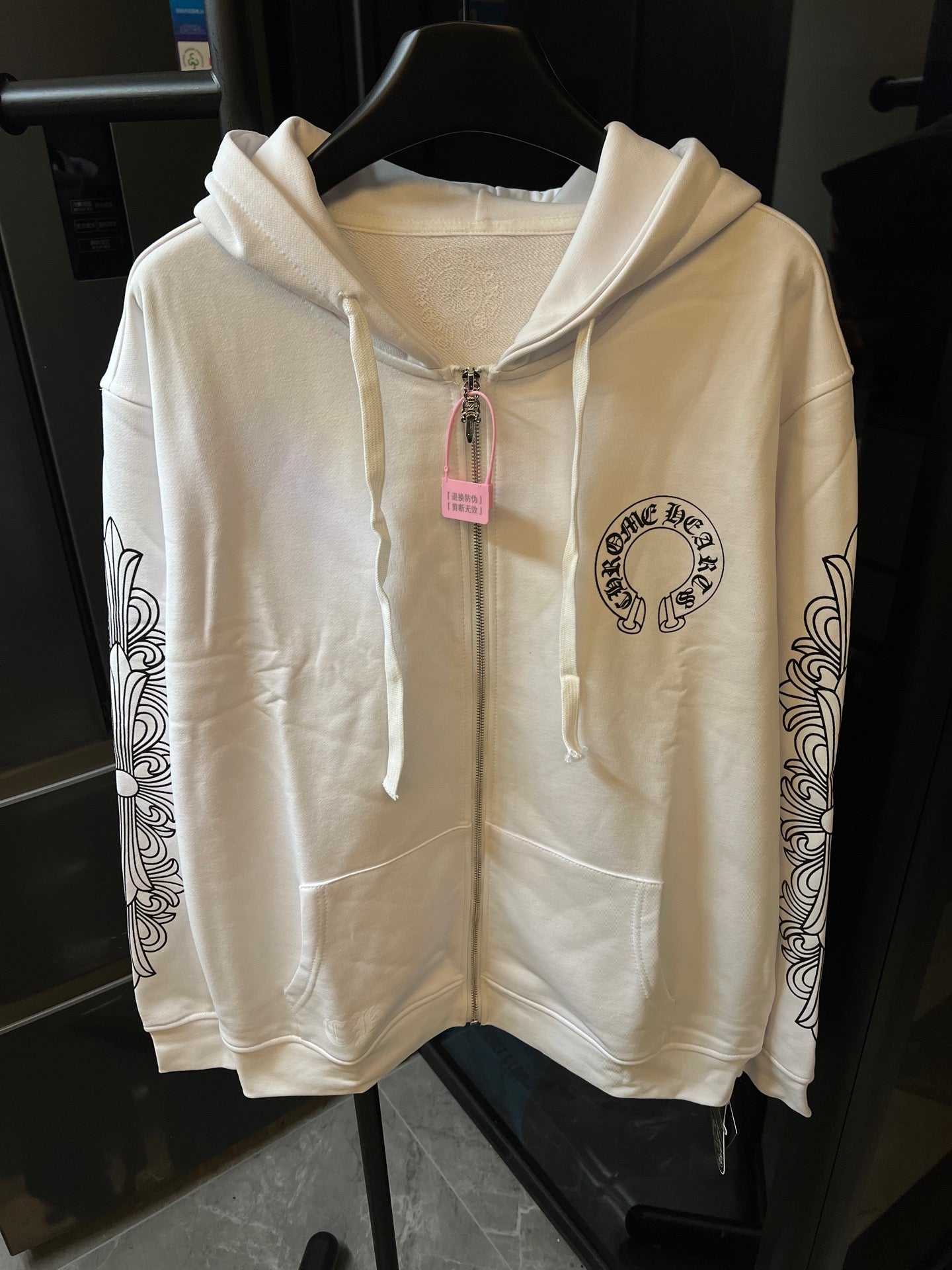 Light cream zip-up hoodie with hood, drawstring, and circular chest logo.