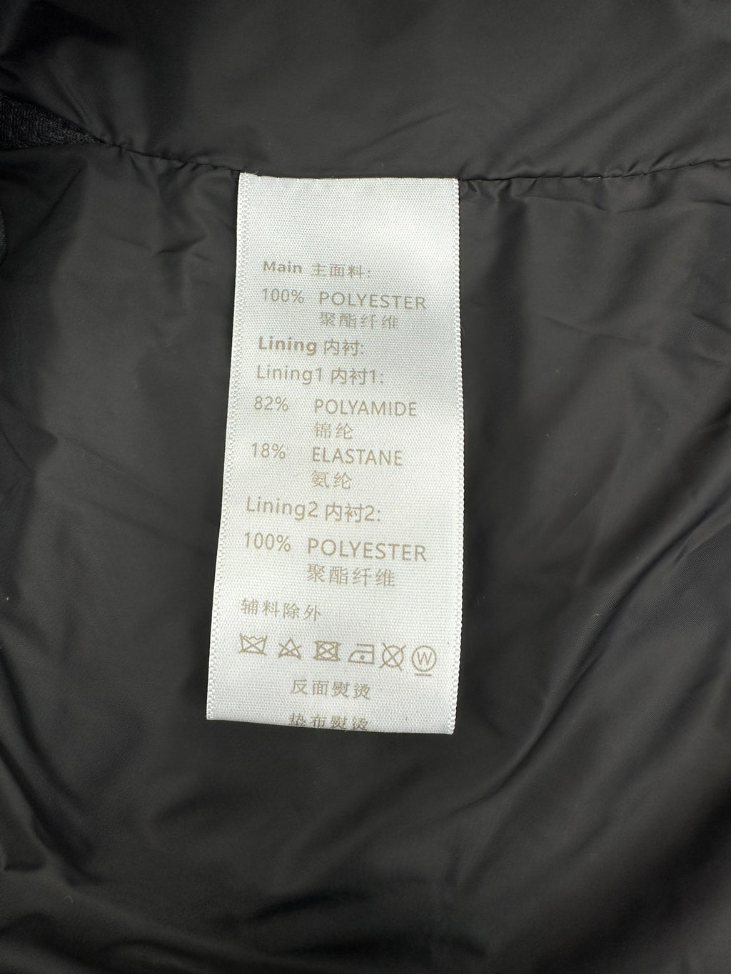 Polyester and elastane care label inside dark Louis Vuitton puffer jacket.