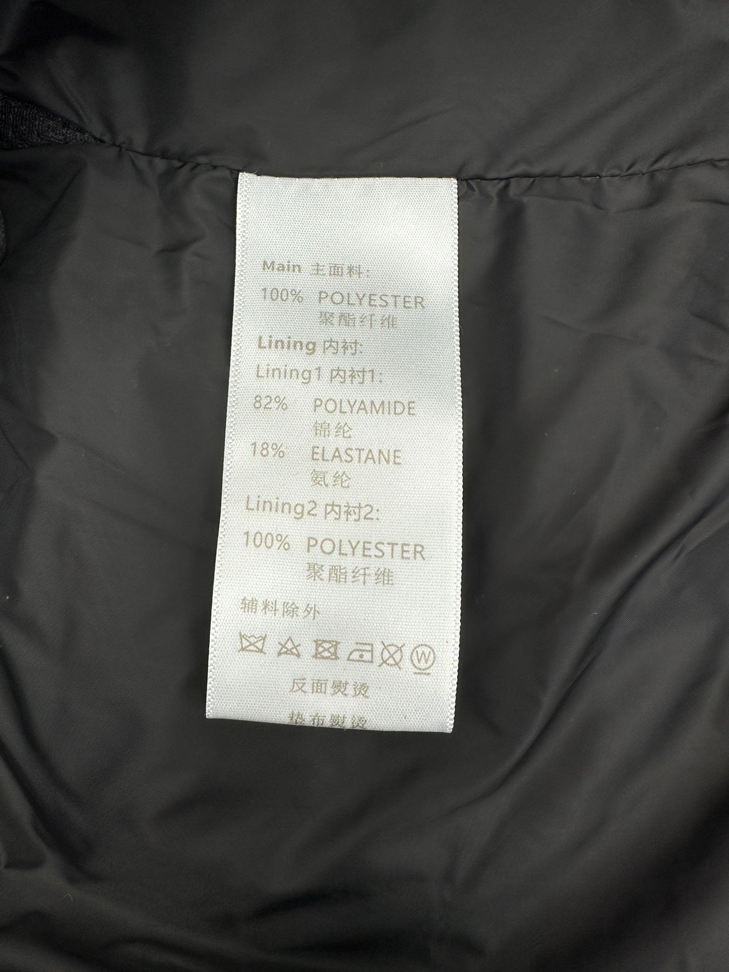 Polyester and elastane care label inside dark Louis Vuitton puffer jacket.
