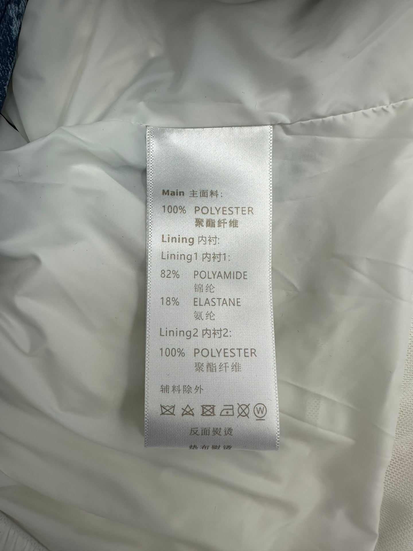 White garment label listing 100% polyester shell and lining, with elastane and polyamide