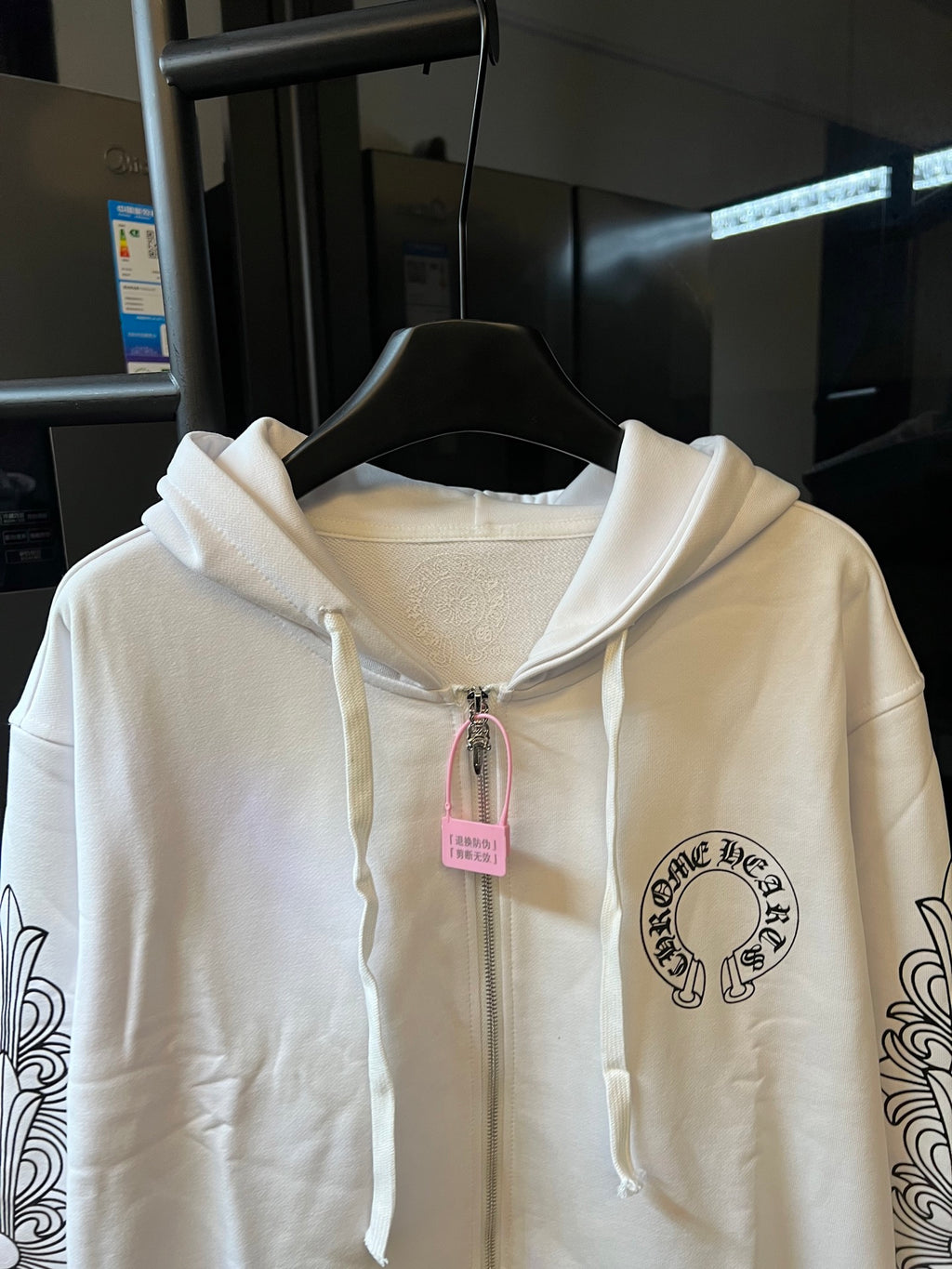 Light cream zip-up hoodie close-up with hood drawstrings and chest emblem.