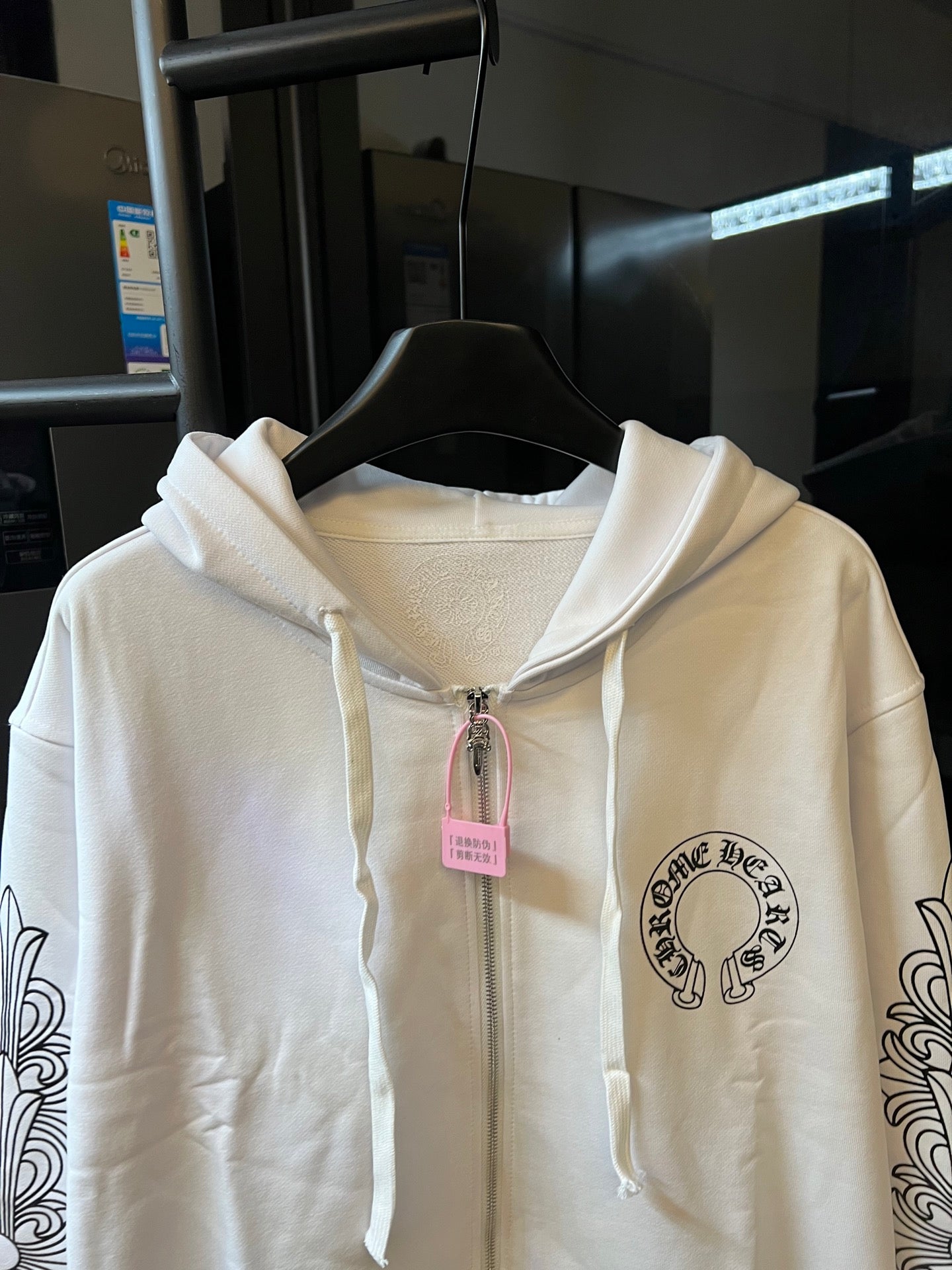 Light cream zip-up hoodie close-up with hood drawstrings and chest emblem.