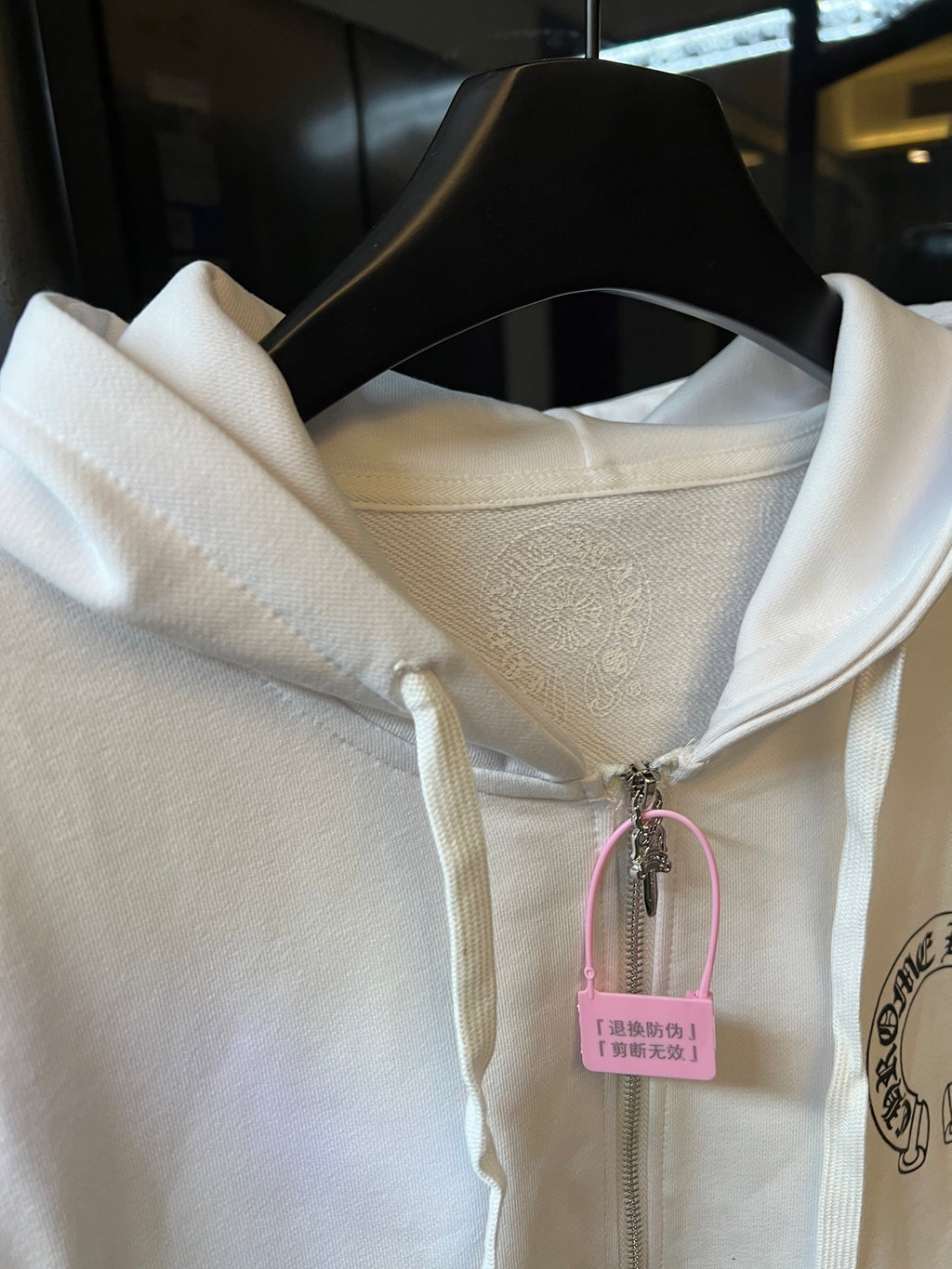 Light cream zip-up hoodie neckline with hood and drawstring, hanging product tag.