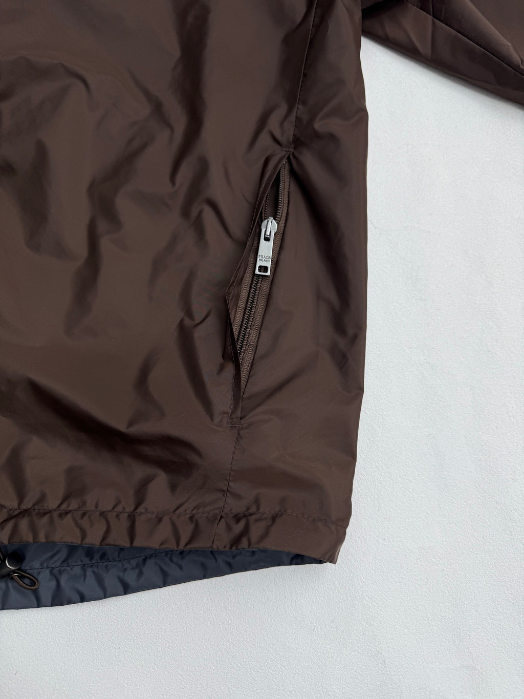 Brown jacket front with silver zipper and blue-lined cuff hem