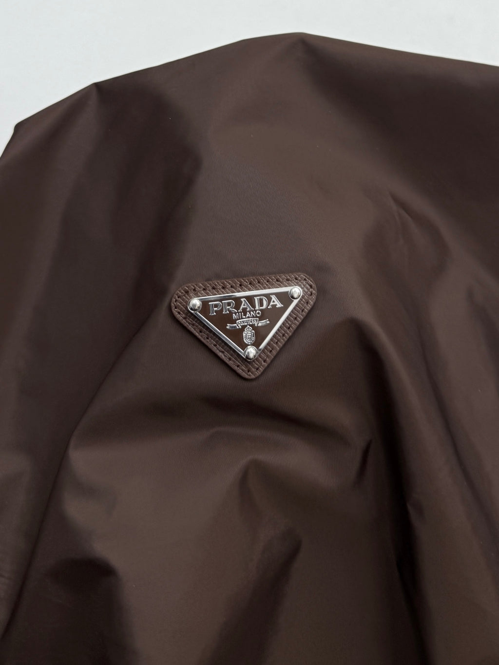 Brown jacket shoulder with triangular Prada logo patch detail