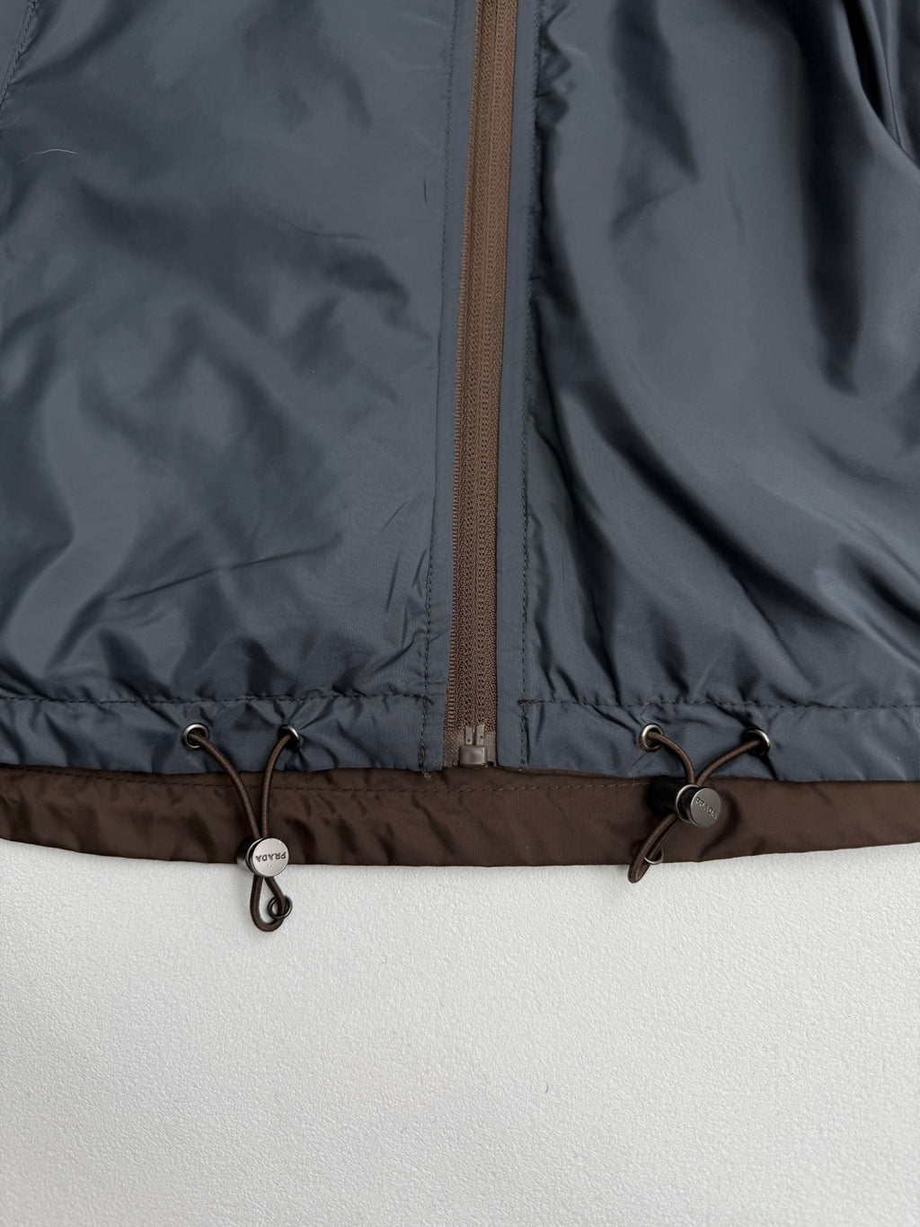 Prada hooded long jacket, blue-gray, hem drawstring toggles and zipper close-up