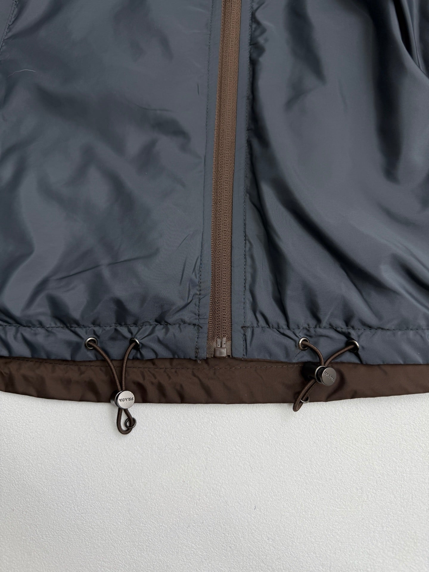 Prada hooded long jacket, blue-gray, hem drawstring toggles and zipper close-up