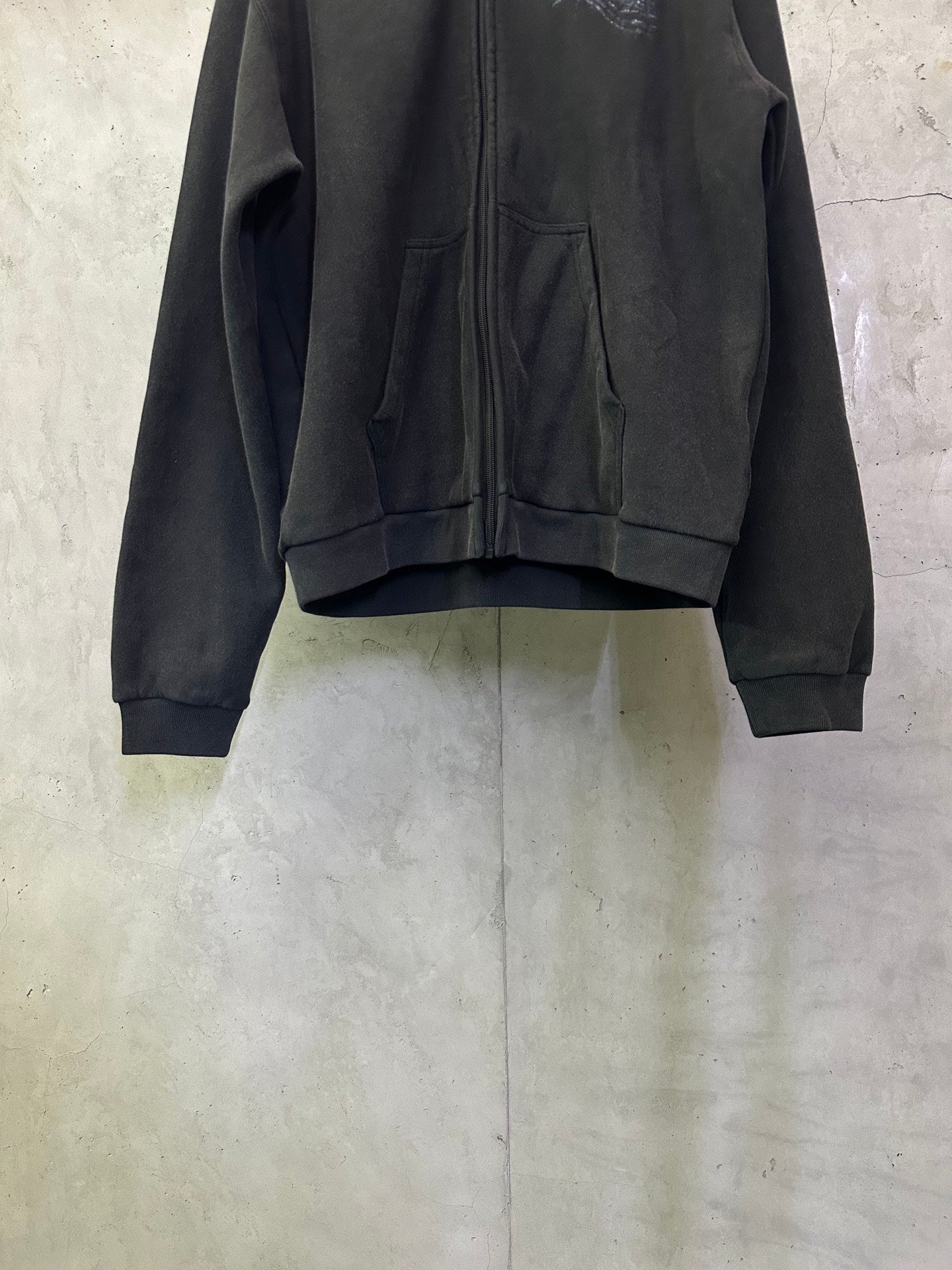 Dark zip-up hoodie front with two pockets and gathered fabric at hem