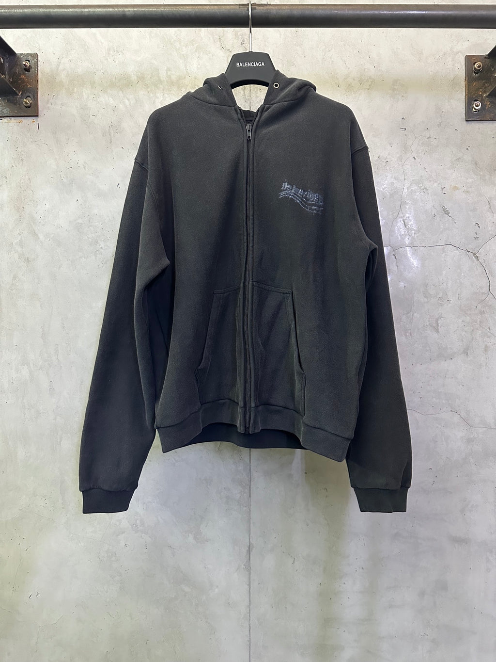 Dark zip-up hoodie with hood, front pockets, and small chest logo print