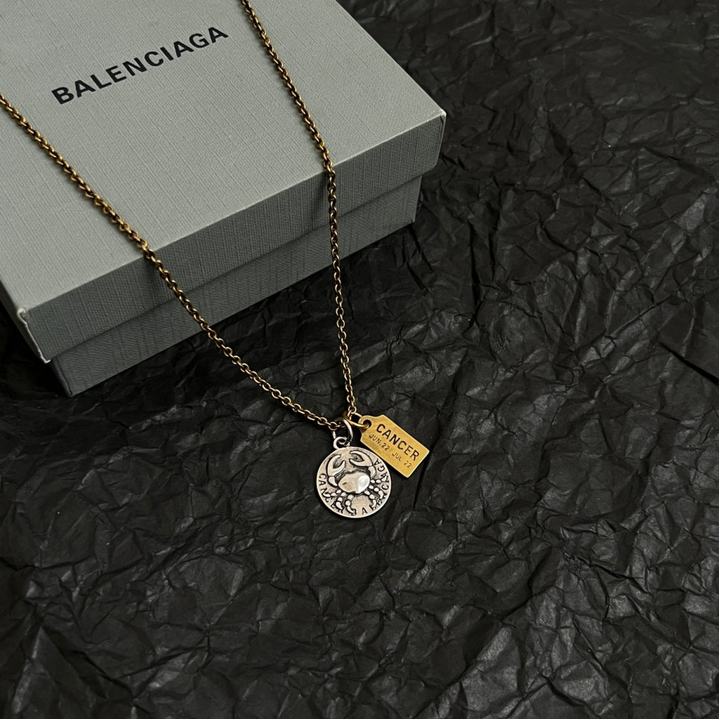 Gold chain necklace with round silver medallion and Cancer charm on black surface